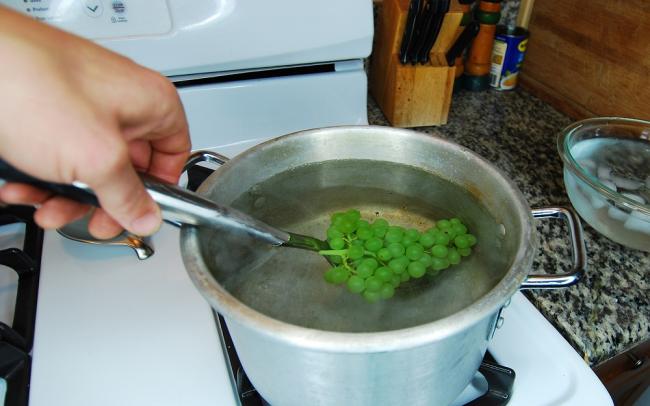 Бланшировка винограда перед сушкой Человек опускает ветку винограда в кипяток