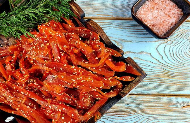 Кальмар вяленый с кунжутом На голубом деревянном столе тарелка с кальмаром в кунжуте