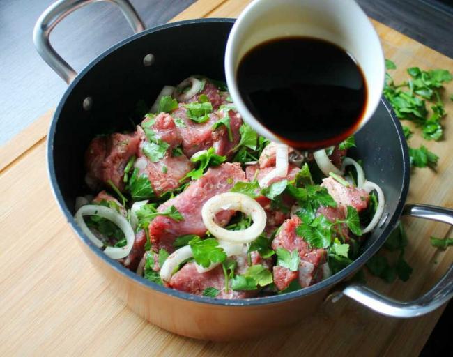 Куски свинины поливают соевым соусам  Кастрюля с кусками свинины и лука поливают соевым соусом